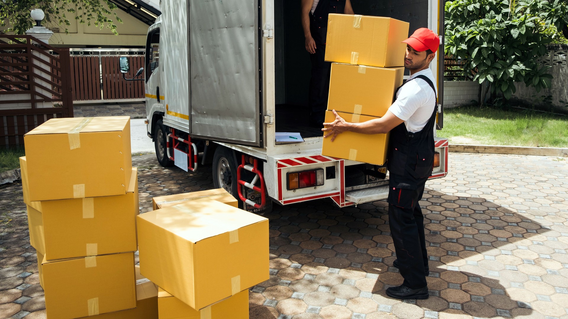 Asian and Caucasian workers in uniform unloading cardboard boxes from the truck. Delivery men unloading boxes and check the checklist with their coworkers. Professional delivery and moving service.